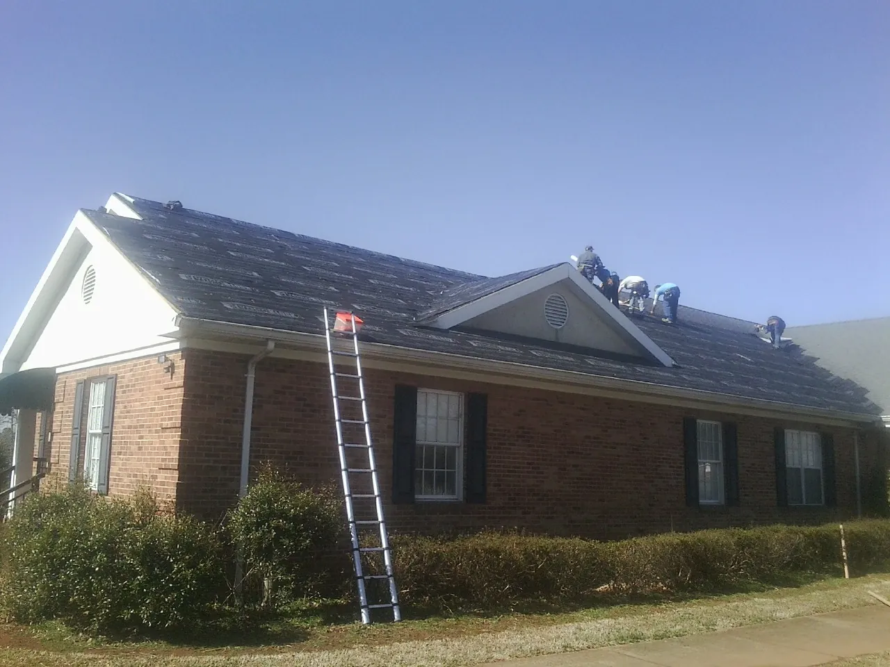 Crew tearing shingles off a brick ranch roof with a ladder set — Emergency Roof Repair work by our crew in Chrisney