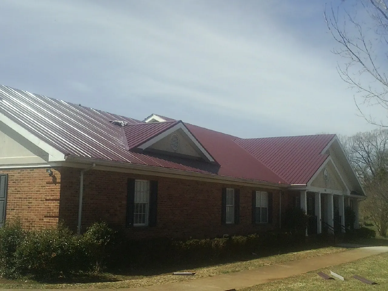 Red metal roof with gabled entries on a long brick building, from a Hail Damage Roof Repair job in Chrisney