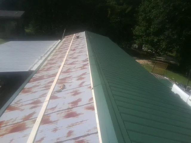 Old rusted panels beside newly installed green metal roofing — Wind Damage Roof Repair by Roofing Brothers in Chrisney