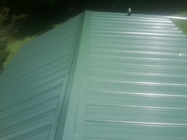 New green metal panels meeting at the ridge of a roof — Flat Roof Repair work by our crew in Chrisney
