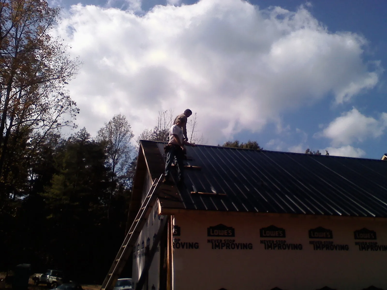 Roofer fastening dark metal panels high against a cloudy sky, from a Roof Inspection job in Chrisney