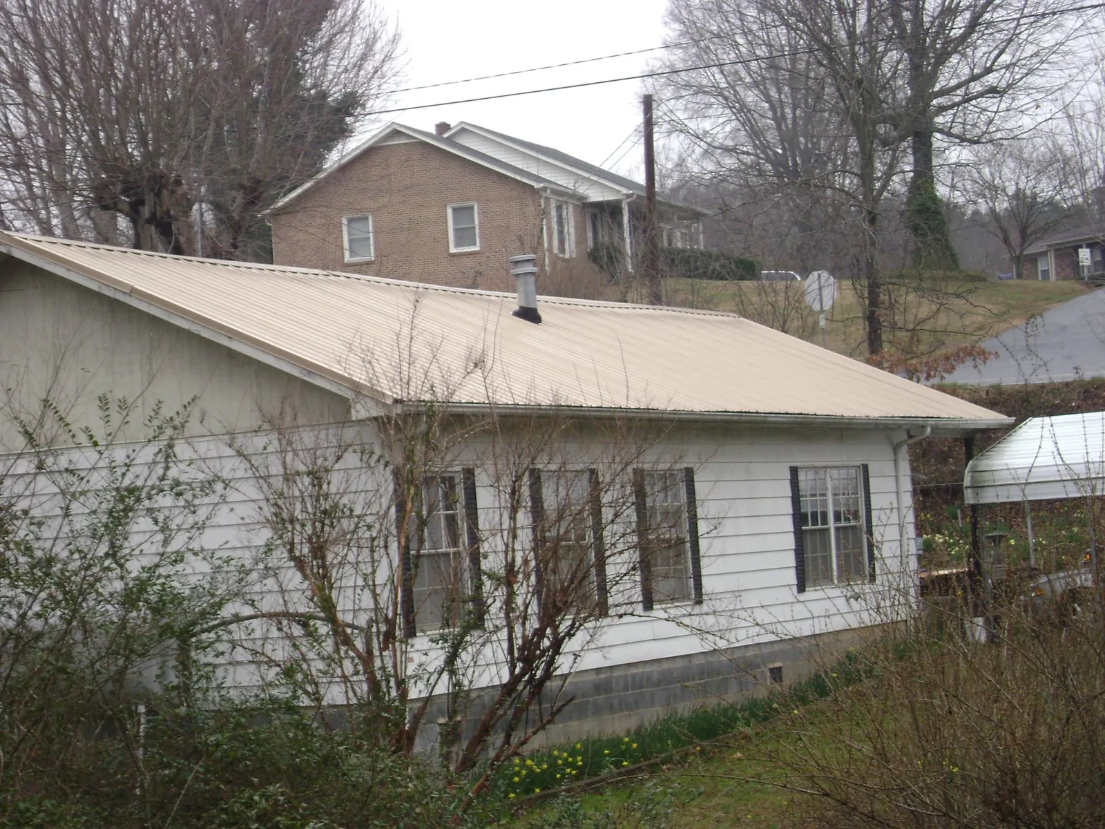 Tan metal roof on a white sided house set into a hillside — Commercial Roofing by Roofing Brothers in Chrisney